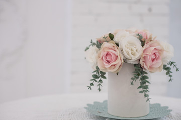 Bulk artificial flowers in a round box are on the table. Artificial flowers on a white background