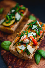 Italian bruschetta with chopped vegetables on toasted crusty baguettes sprinkled with parmesan and chives on rustic wooden board