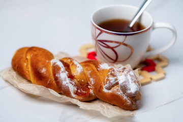 sweet bun with icing sugar next to a cup of tea