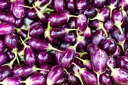 Close up of small purple Asian eggplants. Top view of fresh organic eggplants or brinjal at street market. Purple vegetable background 