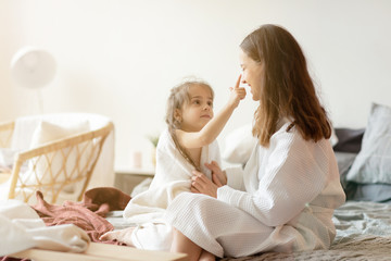 Daughter and mother in playful mood sitting on bed  in bedroom after shower. 