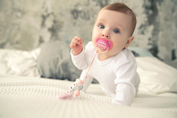 A baby with a pink pacifier in her mouth crawls on the bed.