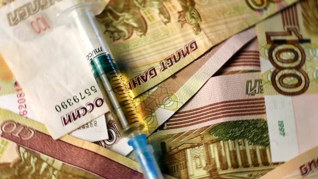 Medicine and money. A filled syringe lies on the money.