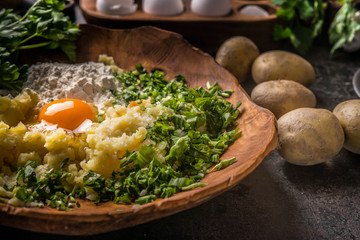 Close up of preparation of gnocchi dough ingredients. Potatoes with egg and flour in wooden bowl on dark kitchen table with ingredients. Tasty home cooking.   Top view. Copy space