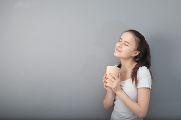 Aromatic coffee in a glass with you. Young woman drinks hot drink on gray background