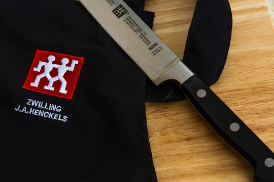 Illustrative editorial of Zwilling J.A. Henckels kitchen knife and black apron with logo on wooden chopping board
