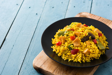 Fried rice with chicken and vegetables on black plate on blue wooden table. Copy space	