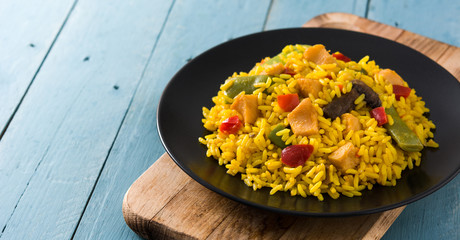 Fried rice with chicken and vegetables on black plate on blue wooden table	