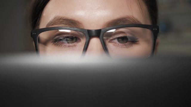 Woman works at laptop. Close-up of female eyes in glasses looking at computer screen during work. Close up