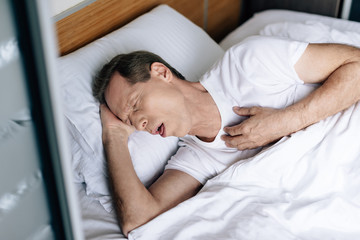 overhead view of sick man coughing while lying on bed