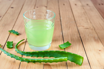 A glass of aloe drink juice and green aloe leaves on a wooden background.