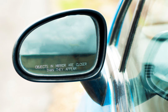 The inscription on the car side mirror: "Objects in mirror are closer than they appear", closeup. A concept of warning, safety and care for the driver. Car's Reflection In Rear View Mirror. 