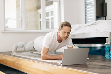 man exercising on fitness mat while watching online working out on laptop © LIGHTFIELD STUDIOS