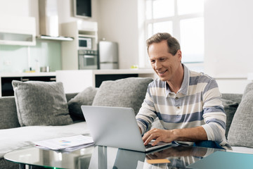 Obraz premium cheerful man smiling while using laptop near credit card in living room