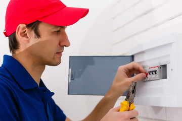 Young adult electrician builder engineer screwing equipment in fuse box