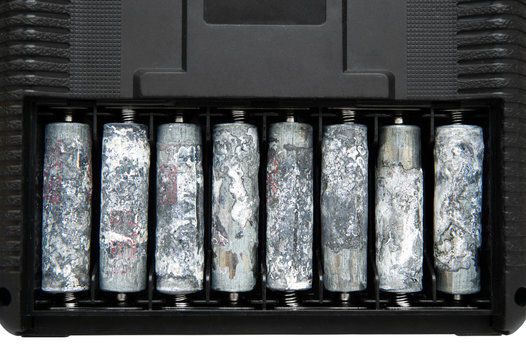 A Row Of Eight Unwrapped And Heavily Oxidized AA Batteries Inside The Battery Compartment Of An Electronic Device.