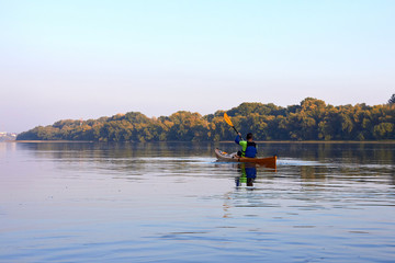 Obraz na płótnie Canvas Kayaking in the Danube river at sunset at calm early autumn day. Man paddle at the yellow kayak