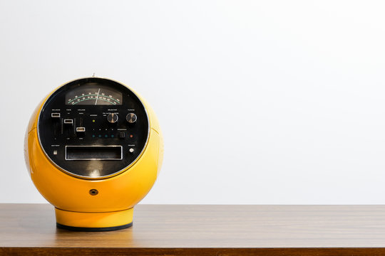 Retro old outdated classic yellow radio receiver from circa 60s century on wooden stand with white wall background. Vintage style filtered photo