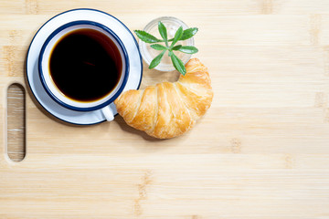 Cup of black coffee espresso and croissant for breakfast on wooden background with coffee beans and leaf, Mockup for design and copy space.