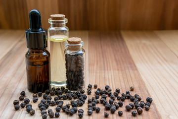Black pepper essential oil bottle with black pepper seed, on wooden board background, health care...