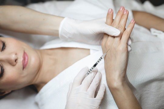 Picture of hands in white gloves hold syringe and inject some botox under hands skin. Take care about young beautiful hands.