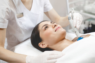Obraz na płótnie Canvas Side view of happy young woman lying on cosmetologist's table during rejuvenation procedure. Cosmetologist take care about neck skin youthfull and wellness.
