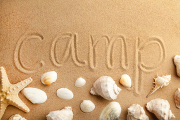 Fototapeta na wymiar Inscription camp with seashells on beach sand.