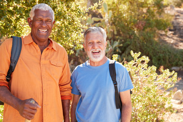 Portrait Of Two Senior Male Friends Hiking Along Trail In Countryside Together
