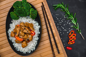 Chinese dish on stone background. Chicken with rice in black plate on wooden board. Horizontal shot.