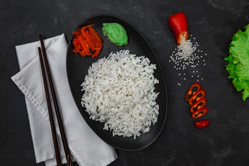 Rice with vegetables and chopsticks on black background. Chinese dish. Horizontal shot.