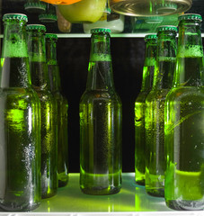 Green beer bottles on the shelf in the refrigerator. The fog on the glass.