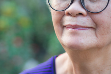 Close-up of half face an elderly woman wearing glasses, smiling and looking at the camera while...
