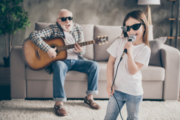 Photo of aged grandpa sitting comfy sofa playing guitar little pretty granddaughter hold mic...