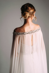Bride wearing white wedding dress with elegant lace cape and shining crystals in photo studio....