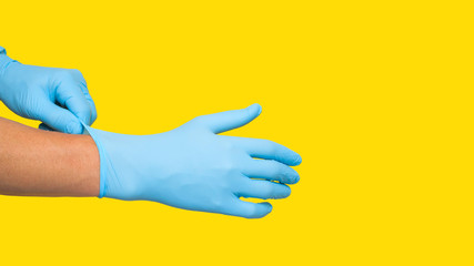 Doctor putting on protective blue gloves isolated on yellow background. Copy space