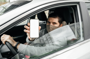 male driver in his car shows a special digital pass document in his smartphone. The concept of free movement around the city in the context of the border pass. mockup.