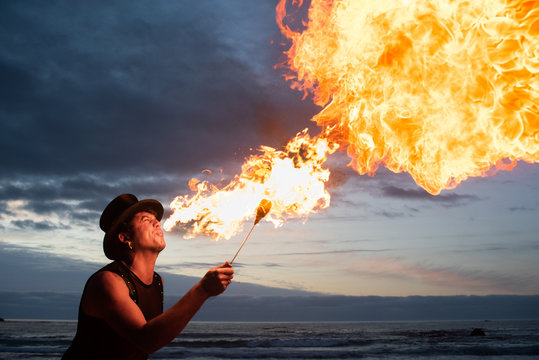 young man fire breathing on the beach at sunset.