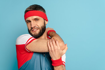 Naklejka premium bearded stylish sportsman warming up arm on blue background