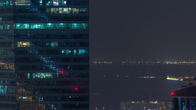 Business bay illuminated office towers at night timelapse. Rooftop view of some skyscrapers near canal and new towers under construction. Traffic on roads and lights in windows