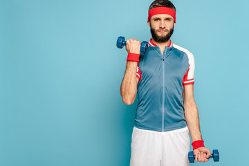 serious stylish sportsman exercising with dumbbells on blue background