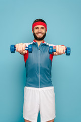 smiling stylish sportsman exercising with dumbbells on blue background