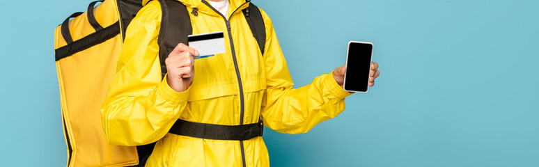 cropped view of deliveryman in yellow uniform with backpack showing smartphone with blank screen...