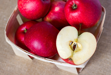 Red apples in a wooden basket box, out of focus and two halves cut with seeds on a homespun linen napkin, summer healthy fruits vitamins, juicy dessert and snack