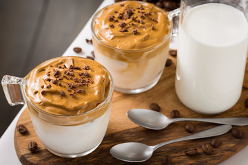 Whipped dalgona coffee and milk jug on table with coffee beans scattered around - ダルゴナコーヒー