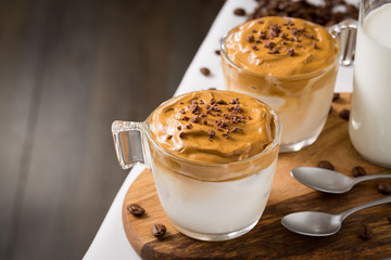 Whipped dalgona coffee and milk jug on table with coffee beans scattered around - ダルゴナコーヒー