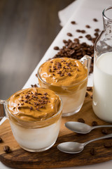 Whipped dalgona coffee and milk jug on table with coffee beans scattered around - ダルゴナコーヒー