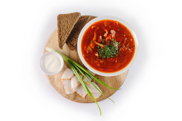 Borscht with sour cream, green onions, bacon and rye bread on a round wooden Board on white background, top view
