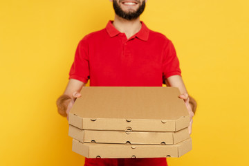 cropped view of smiling bearded delivery man in red uniform with pizza boxes isolated on yellow