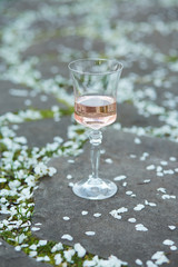 A glass of rose wine on a stone path covered with cherry petals