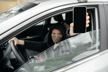 masked woman, a car driver, shows a smartphone screen with a digital pass to travel through the city. The concept of coronovirus epidemic and pandemic.